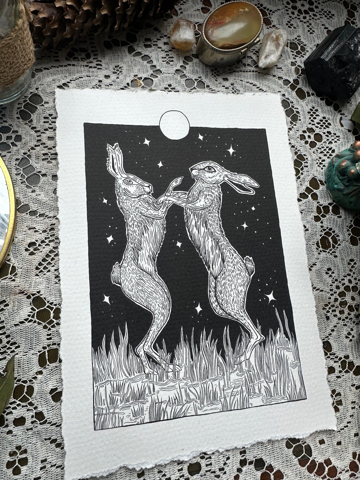 Pen and ink illustration of two hares dancing under the full moon 