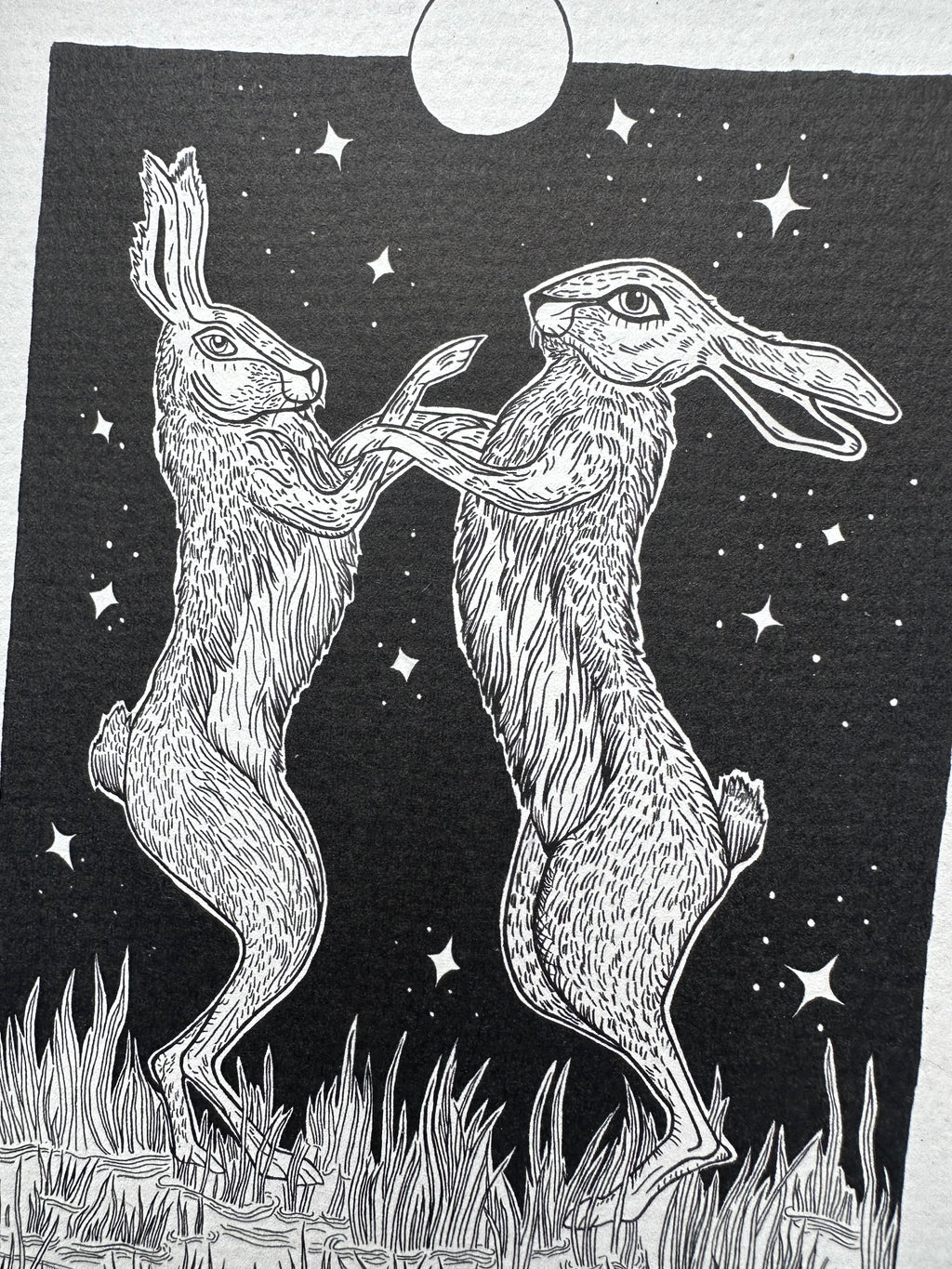 Pen and ink illustration of two hares dancing under the full moon 