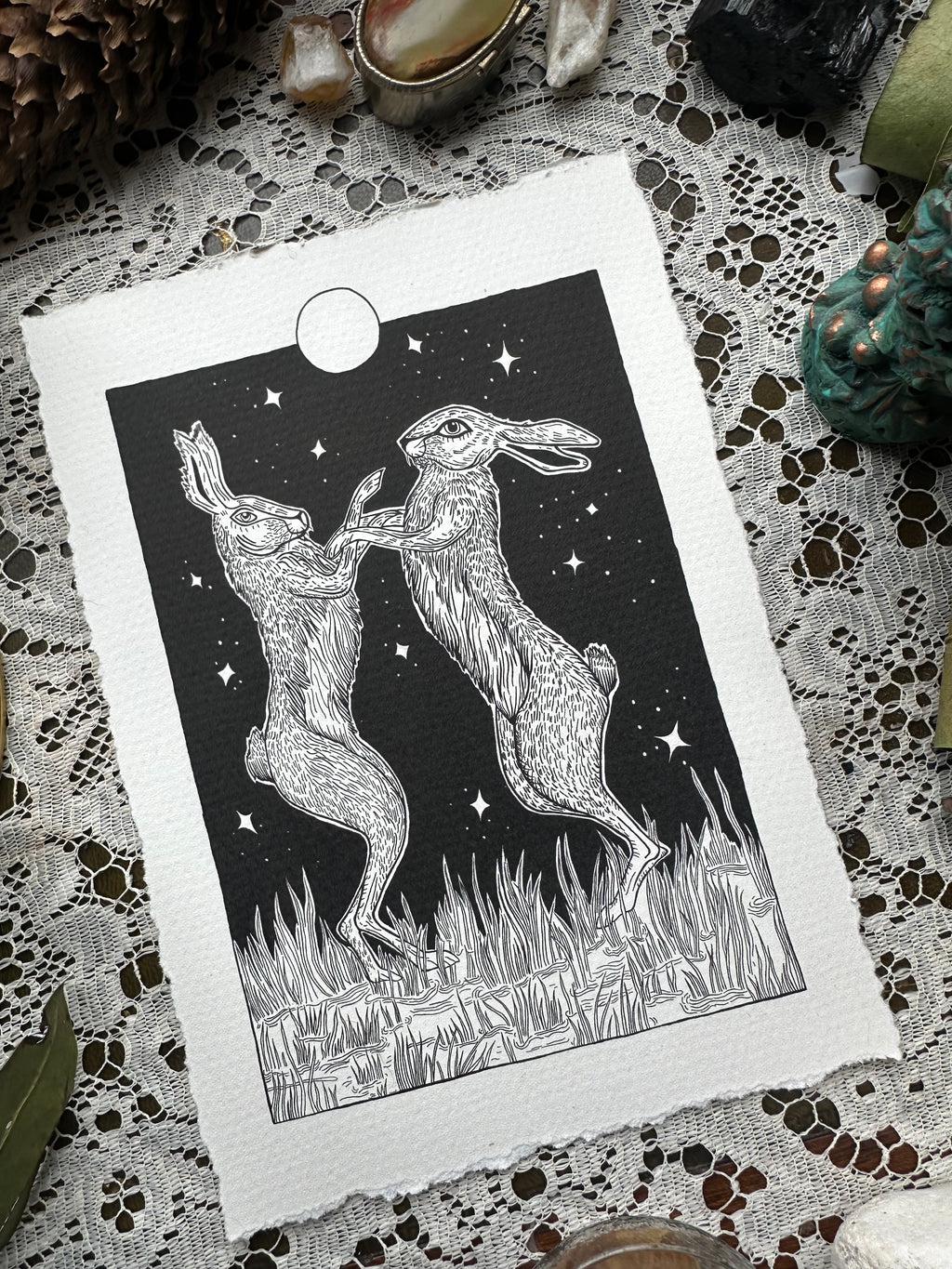 Pen and ink illustration of two hares dancing under the full moon 