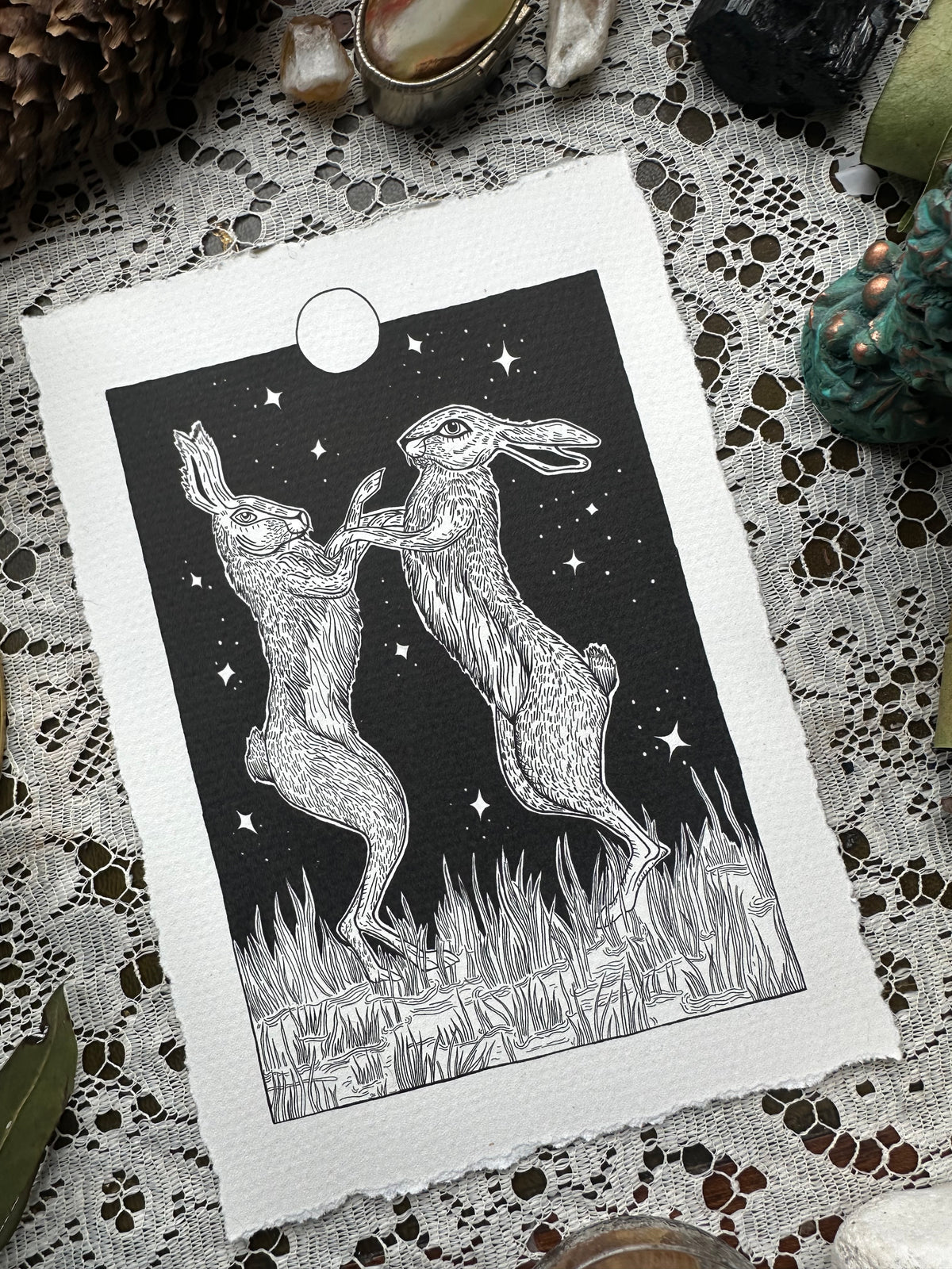 Pen and ink illustration of two hares dancing under the full moon 