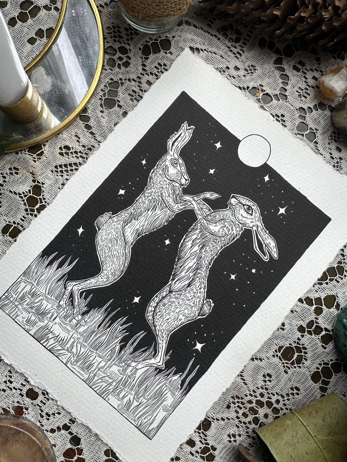 Pen and ink illustration of two hares dancing under the full moon 