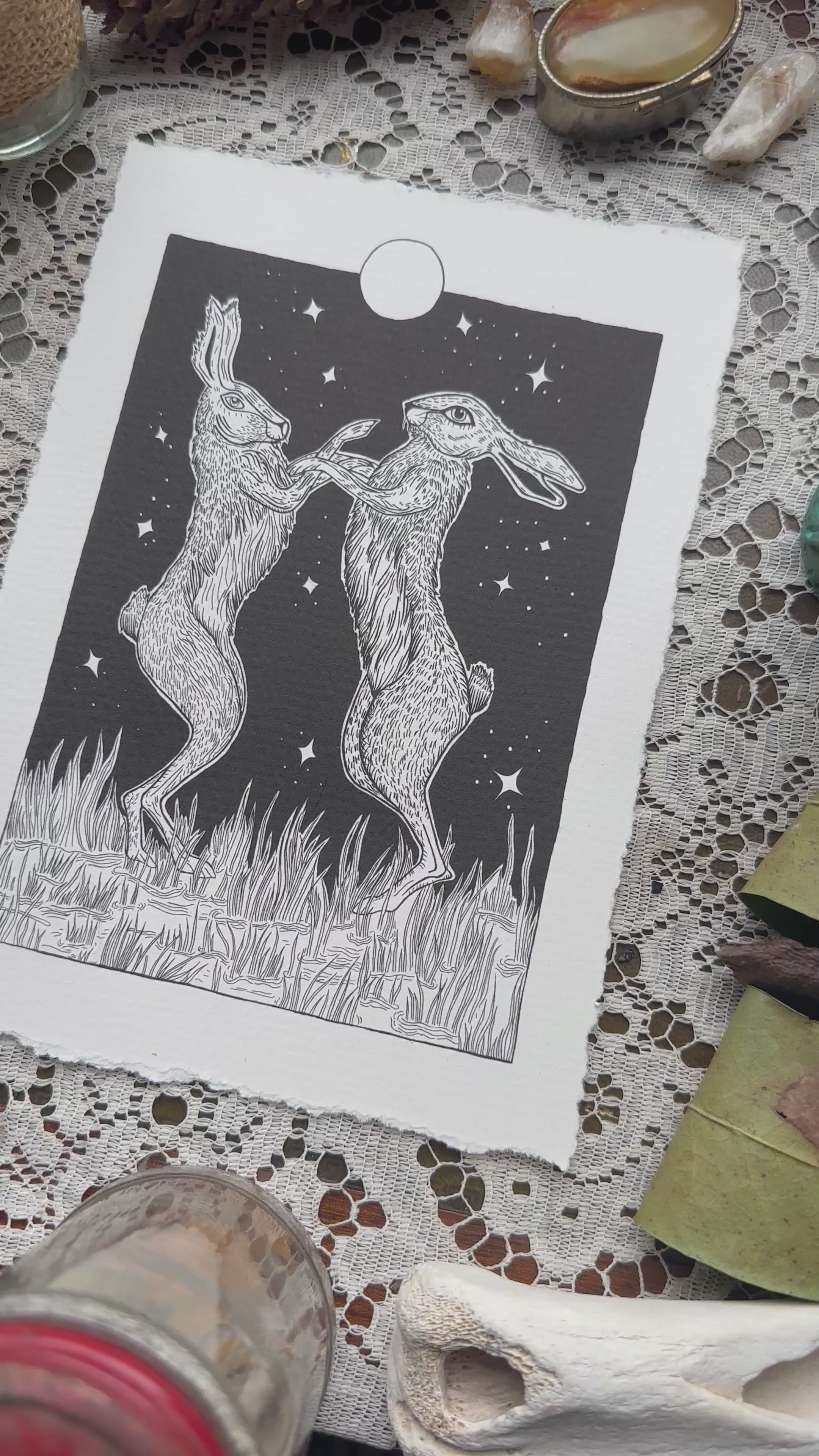 Pen and ink illustration of two hares dancing under the full moon 